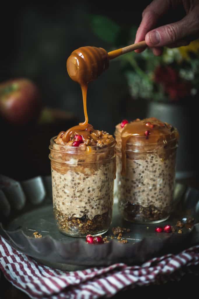 Side view of drizzling caramel onto apple pie overnight oats with a dark, moody background