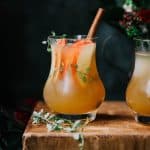 Side view of apple cider bourbon cocktail with sliced apples, thyme and a cinnamon stick