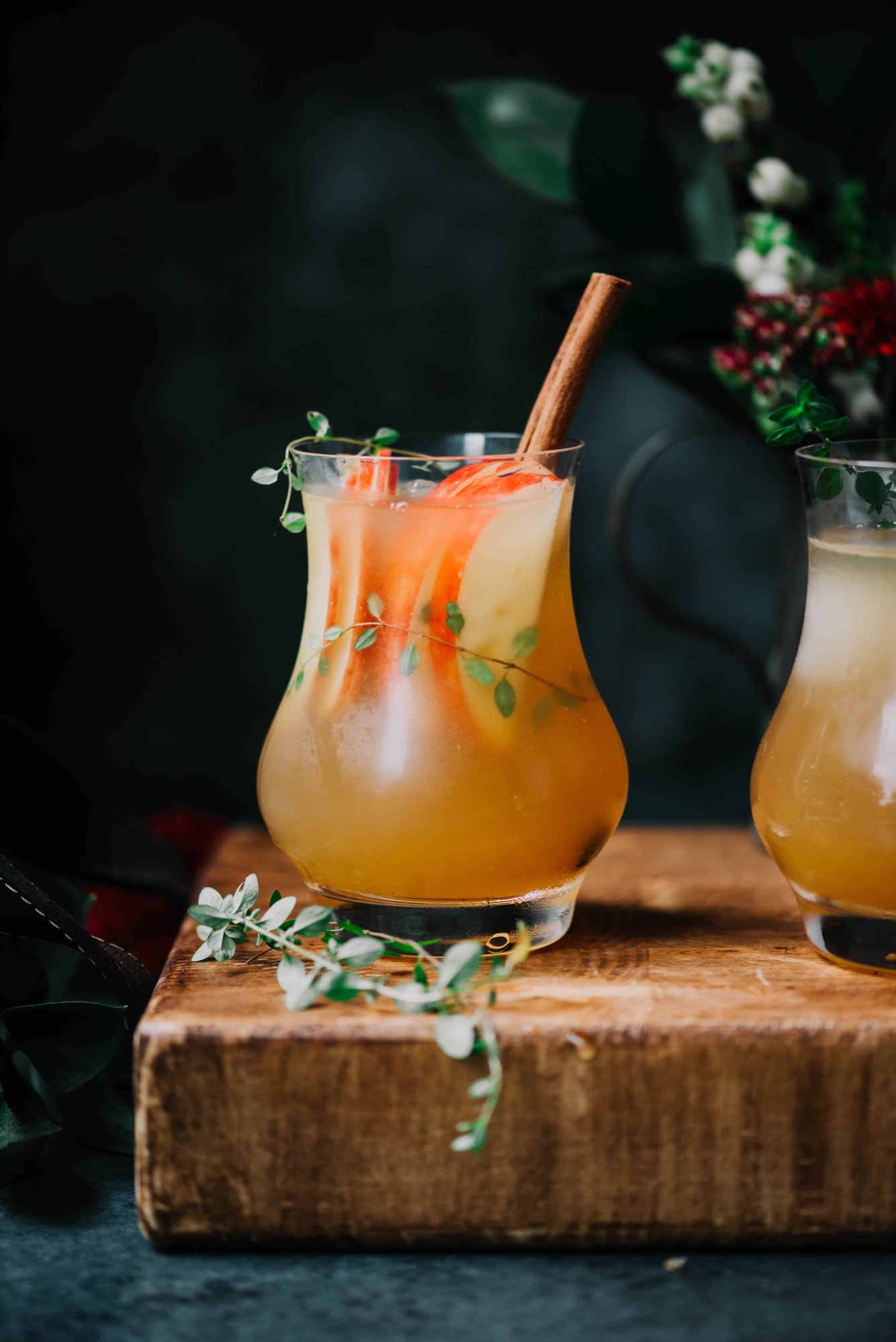 Side view of apple cider bourbon cocktail with sliced apples, thyme and a cinnamon stick