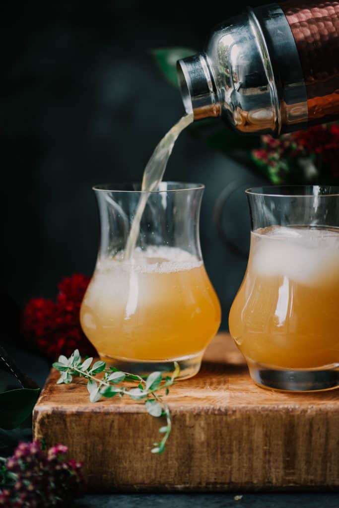 Side view of apple cider bourbon cocktail with sliced apples, thyme and a cinnamon stick
