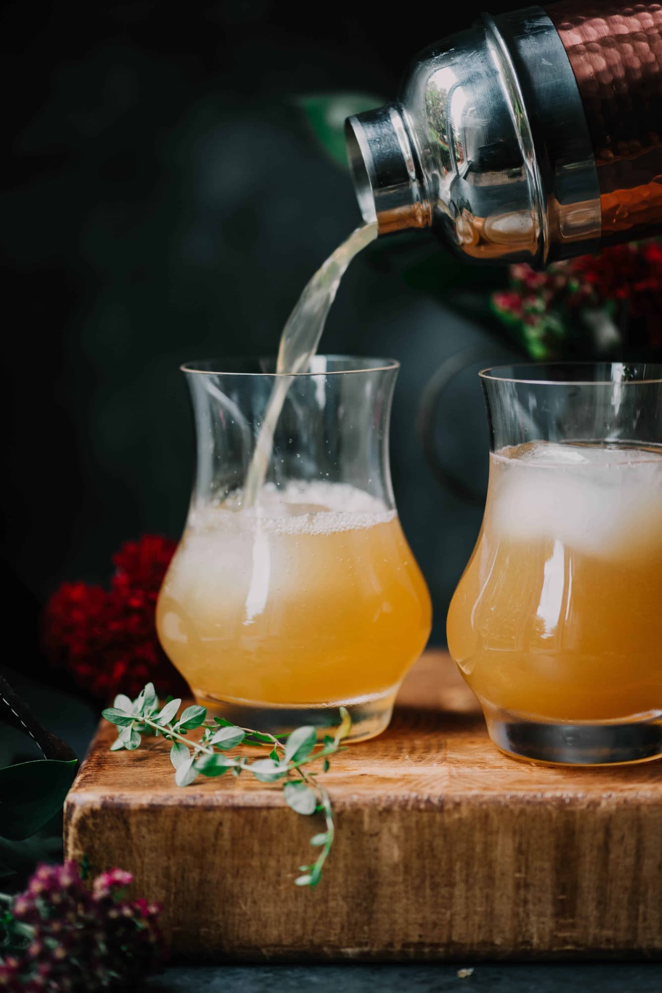 Side view of apple cider bourbon cocktail with sliced apples, thyme and a cinnamon stick