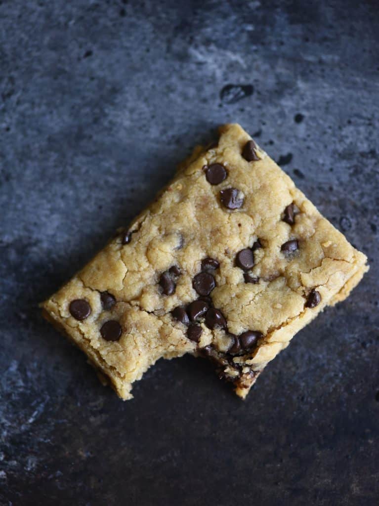 Overhead of chocolate chip cookie bar with bite taken out on a dark background
