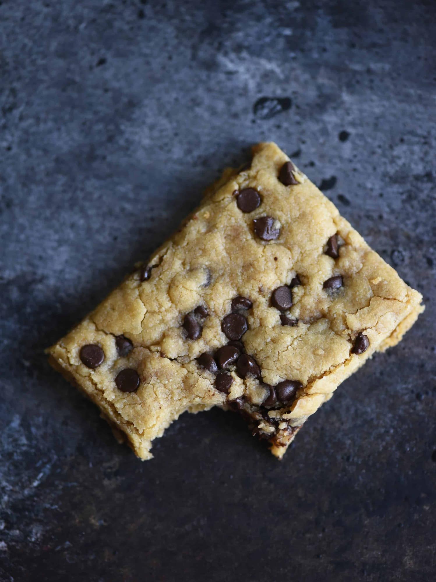 Overhead of chocolate chip cookie bar with bite taken out on a dark background