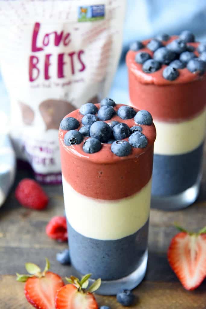 Side view of red white and blue layered smoothies topped with blueberries on a wood background