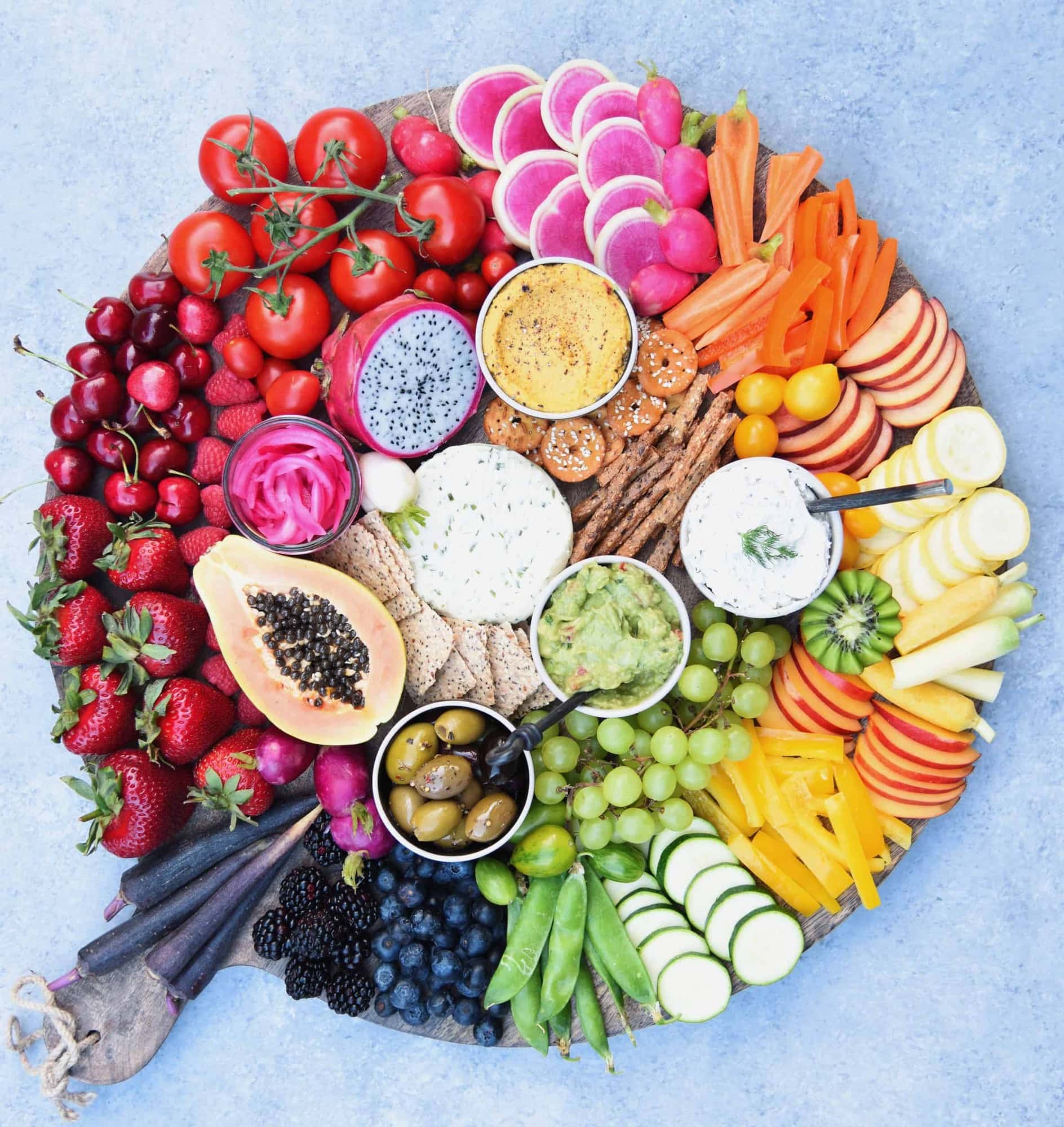 Circular platter filled with rainbow fruits and vegetables, dips and crackers