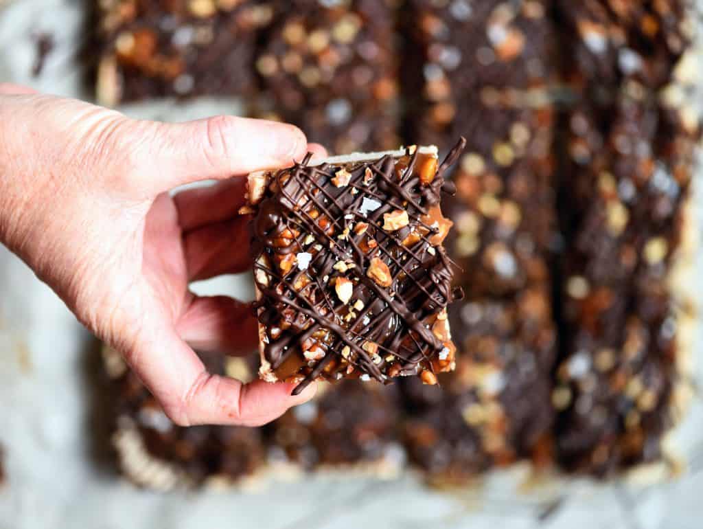 Person holding pecan caramel shortbread bars with drizzled dark chocolate