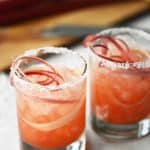 Pouring raspberry rhubarb margarita into glass with rhubarb ribbons