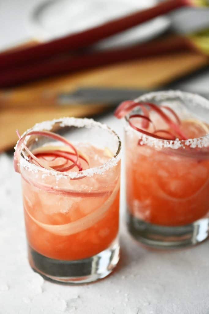 Pouring raspberry rhubarb margarita into glass with rhubarb ribbons