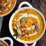 Overhead of curried root vegetable soup in a white bowl garnished with cream and fresh sage