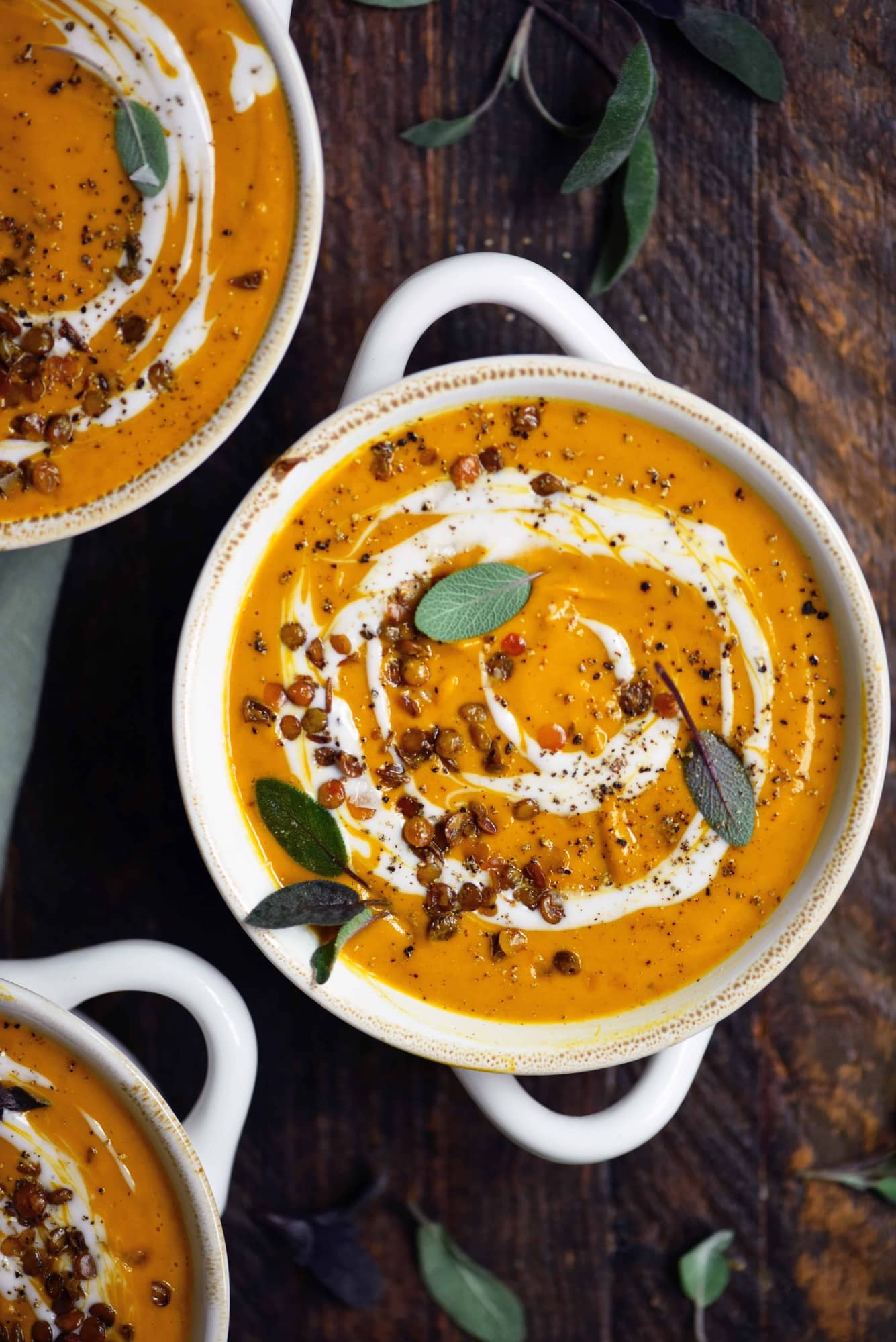 Overhead of curried root vegetable soup in a white bowl garnished with cream and fresh sage