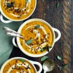 Overhead of curried root vegetable soup in a white bowl garnished with cream and fresh sage