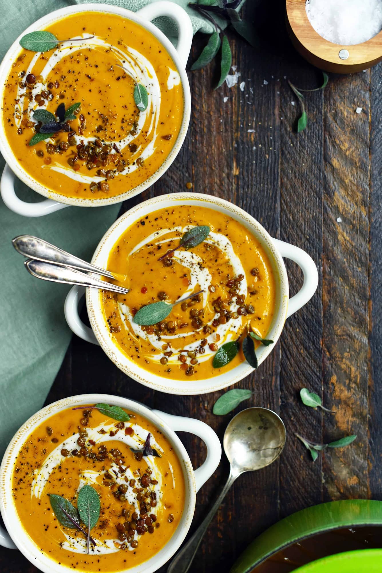 Overhead of curried root vegetable soup in a white bowl garnished with cream and fresh sage