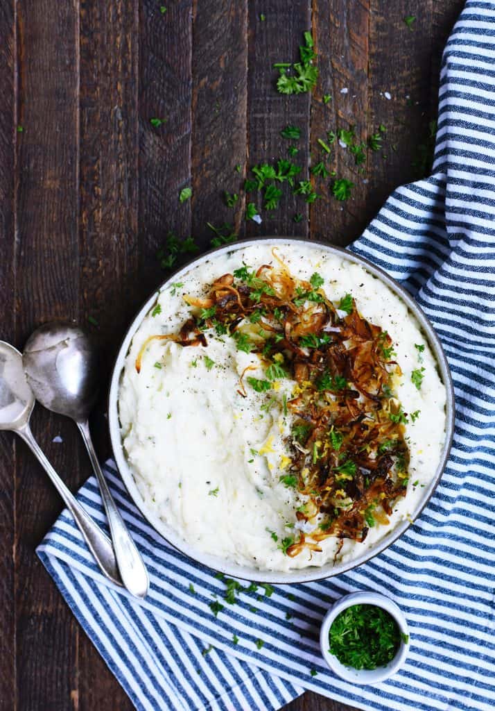 Mashed Potatoes topped with crispy onions and herbs on a striped blue linen