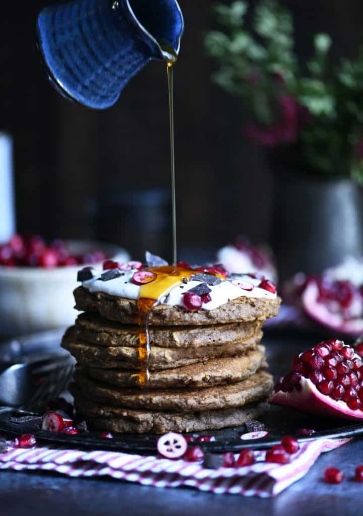 Pouring maple syrup onto a stack of gingerbread oatmeal pancakes with a dark background