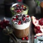 Jars filled with vegan chocolate mousse topped with chocolate and pomegranate on a dark background