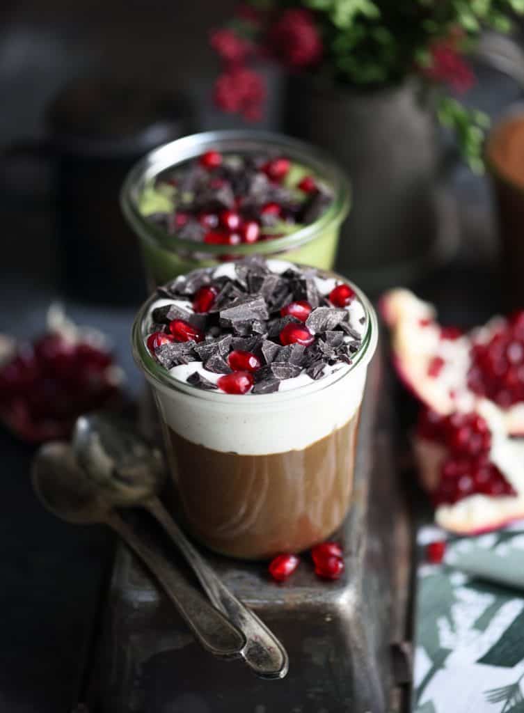 Jars filled with vegan chocolate mousse topped with chocolate and pomegranate on a dark background