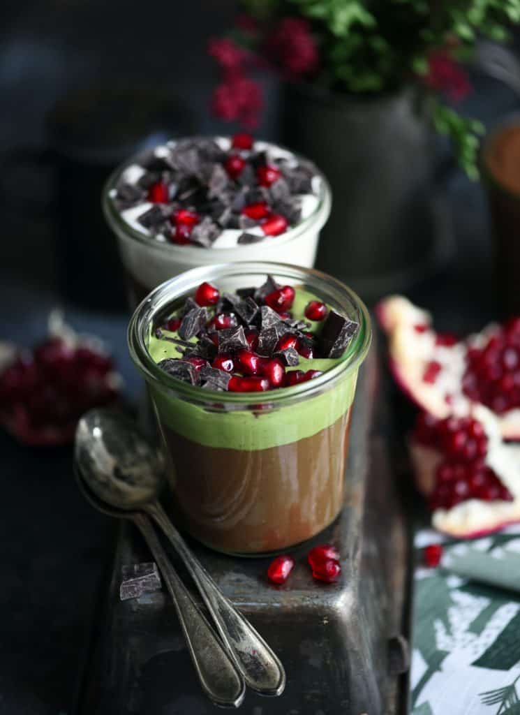 Jars filled with vegan chocolate and matcha mousse topped with chocolate and pomegranate on a dark background