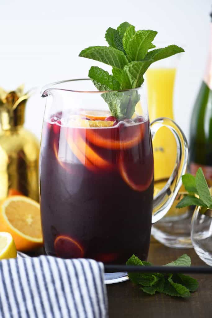 Side view of glass pitcher of holiday punch with citrus and fresh mint
