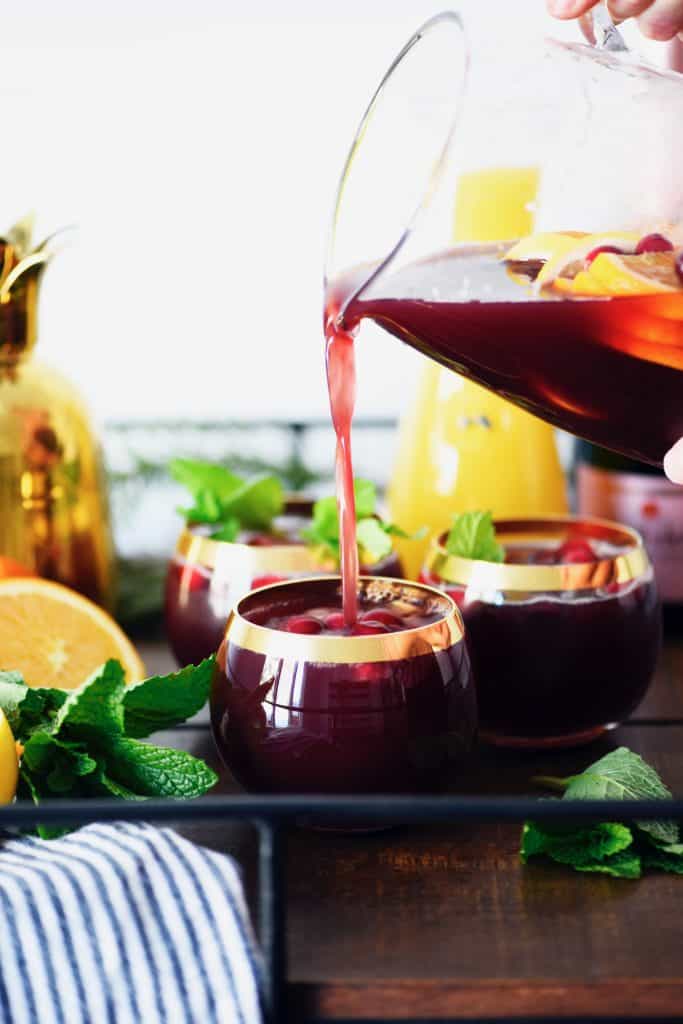 Pouring holiday sparkling punch into glasses on bar cart