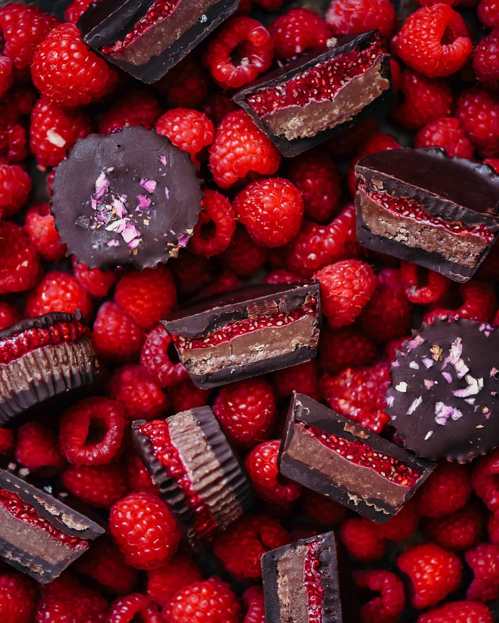 Overhead of chocolate cashew butter cups with raspberry chia jam sliced in half on a bed of fresh raspberries
