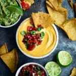Vegan queso in a small white bowl with salsa, guacamole and tortilla chips