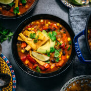 overhead view of vegan tortilla soup in black bowls topped with avocado, tortilla strips and lime.