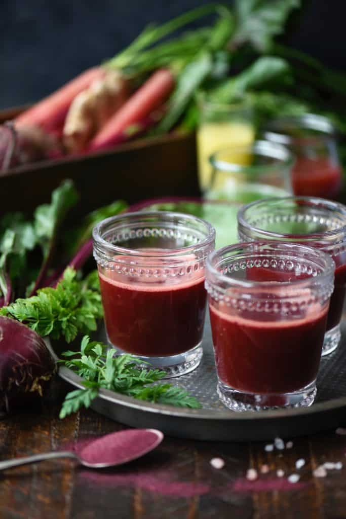 Side view of fresh beet juice in glasses surrounded by fresh vegetables