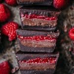 Overhead of chocolate cashew butter cups with raspberry chia jam sliced in half on an antique sheet pan with fresh raspberries