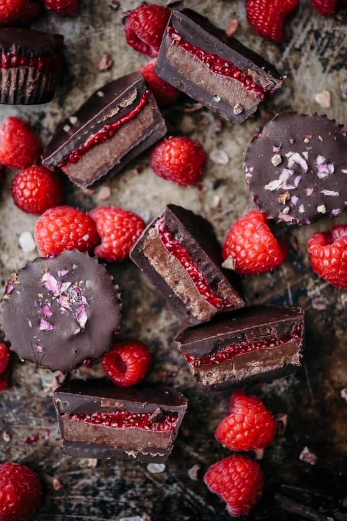 Overhead of chocolate cashew butter cups with raspberry chia jam on an antique sheet pan with fresh raspberries