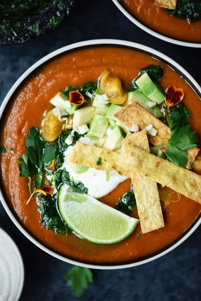 Overhead of fire roasted tomato soup with tortilla strips and avocado