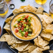 close up overhead view of vegan queso dip in a bowl with tortilla chips around it.