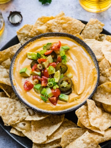 close up overhead view of vegan queso dip in a bowl with tortilla chips around it.