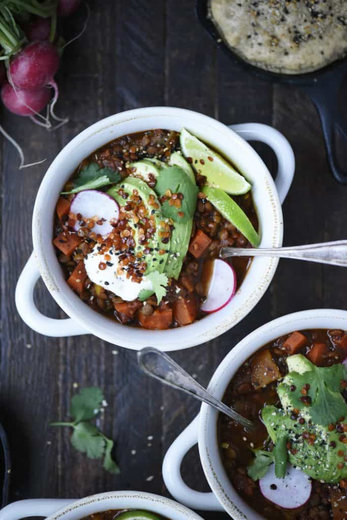Overhead of vegan chili in a white bowl topped with avocado, lime, crispy lentils