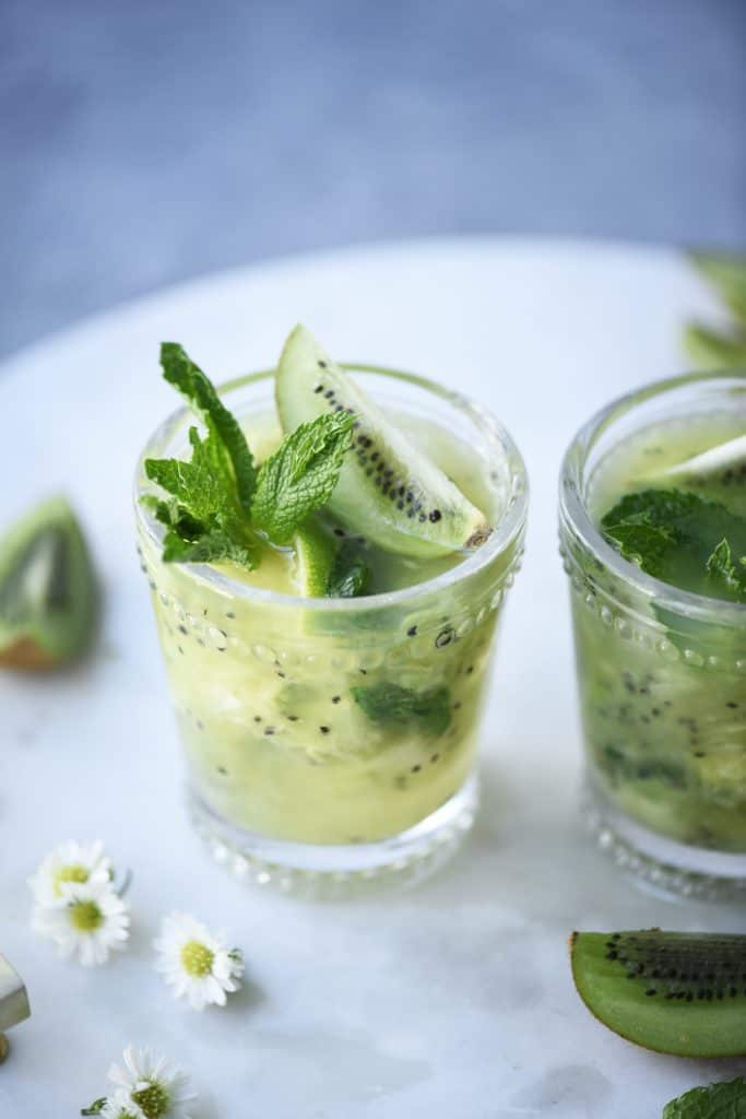 Side view of kiwi caipirinha garnished with fresh mint on a marble serving tray