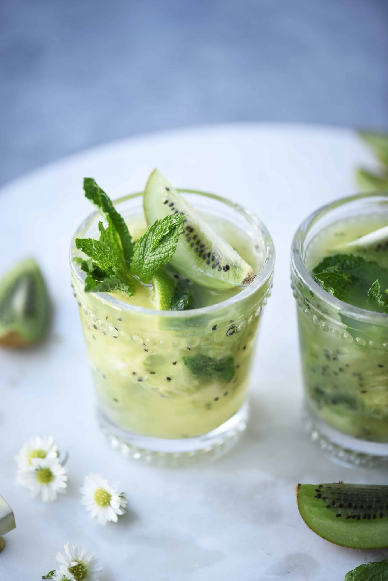 Side view of kiwi caipirinha garnished with fresh mint on a marble serving tray