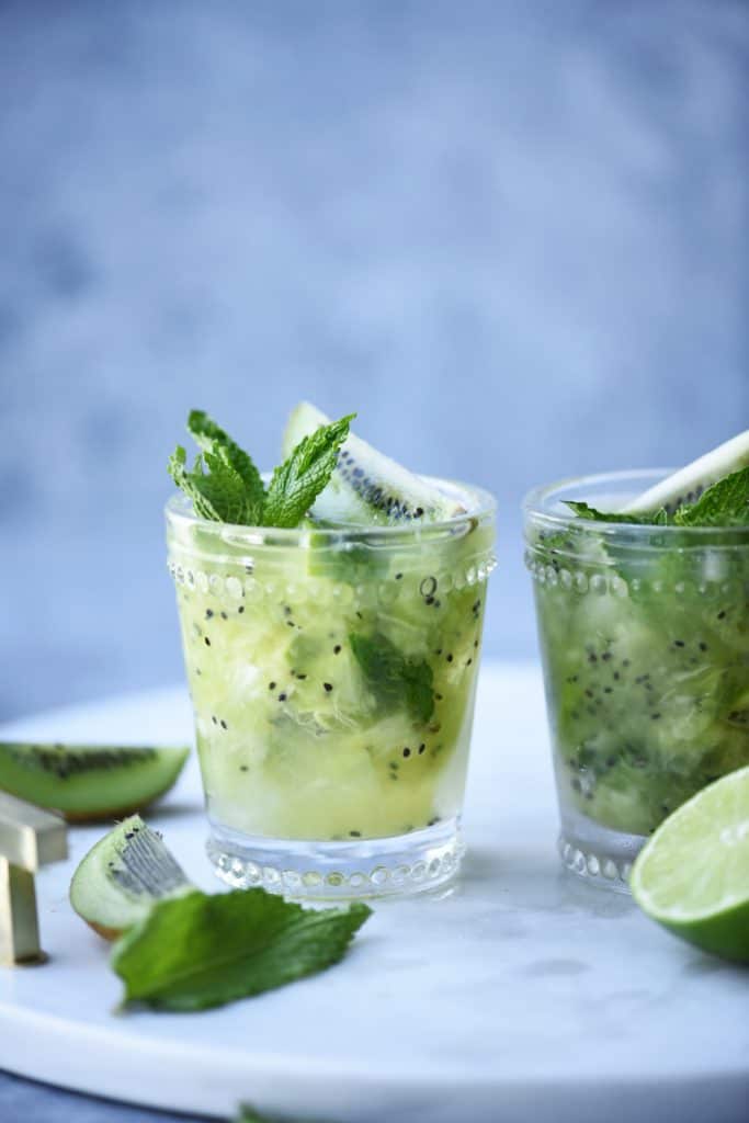 Side view of kiwi caipirinha garnished with fresh mint on a marble serving tray