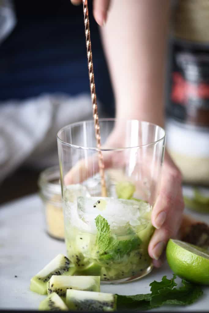 Muddling fresh kiwi and mint in a large glass jar