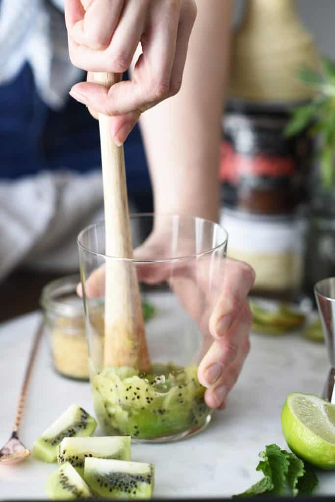 Muddling fresh kiwi and mint in a large glass jar