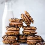 Stack of peanut butter sandwich cookies drizzled with dark chocolate on a white marble background with jug of milk