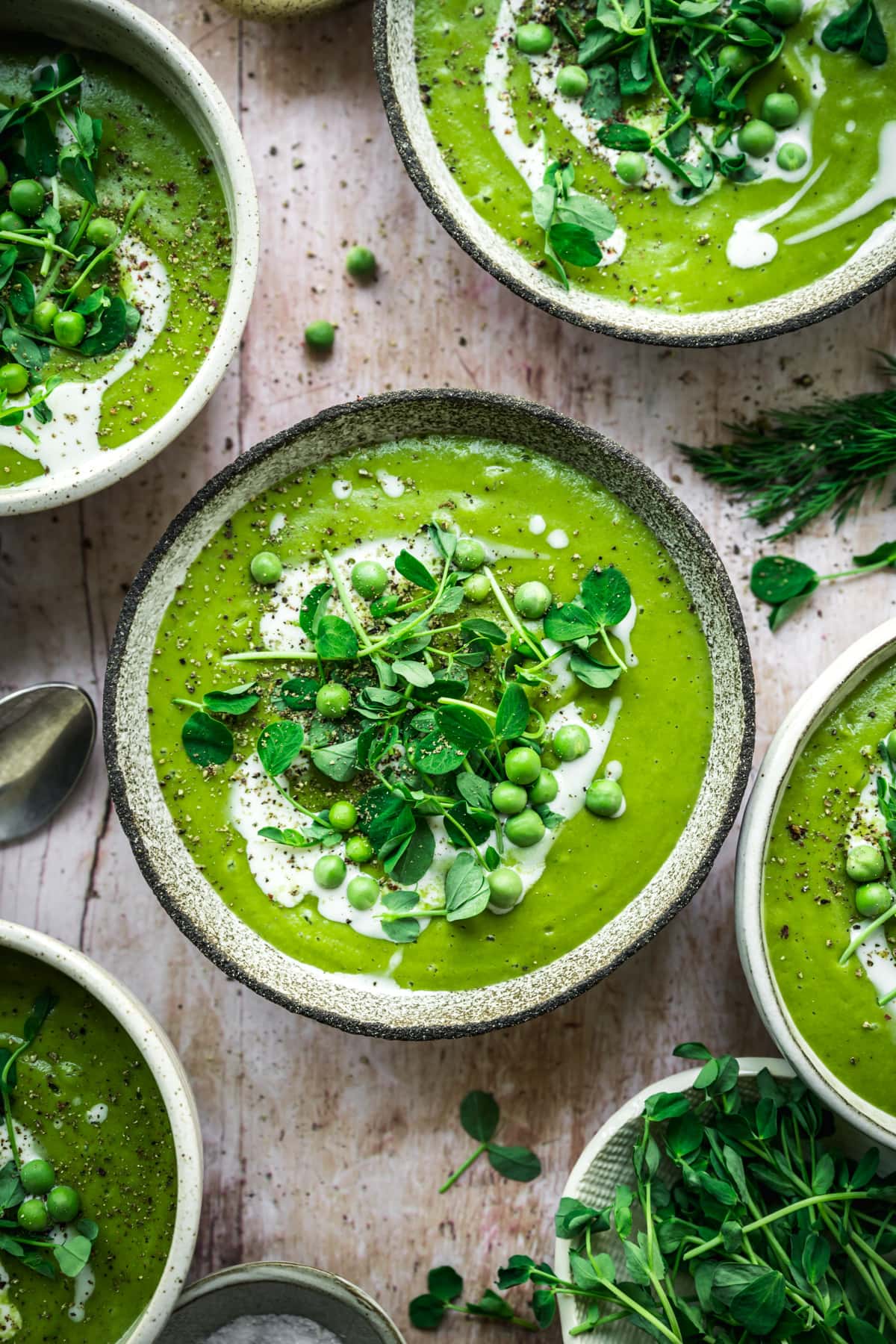 overhead view of vegan asparagus soup with peas in rustic bowl with cream swirl and microgreen garnish. 