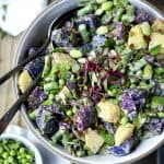 Overhead of purple potato spring salad in a white bowl with microgreens and fresh peas