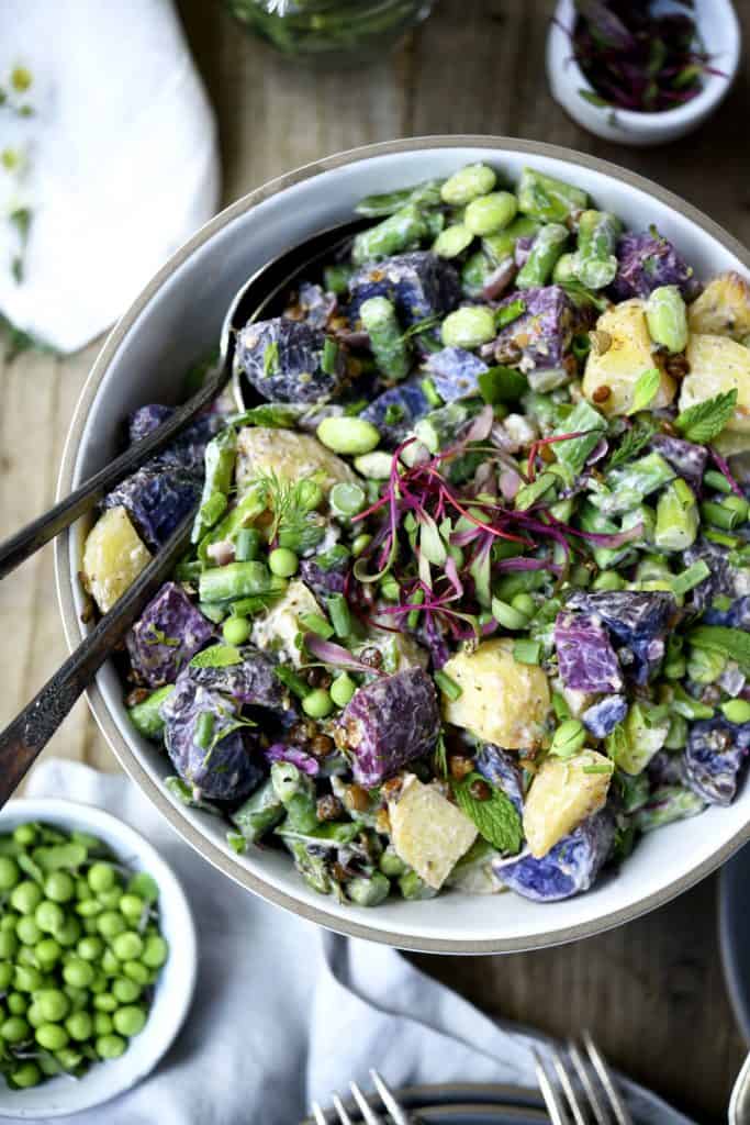 Overhead of purple potato spring salad in a white bowl with microgreens and fresh peas