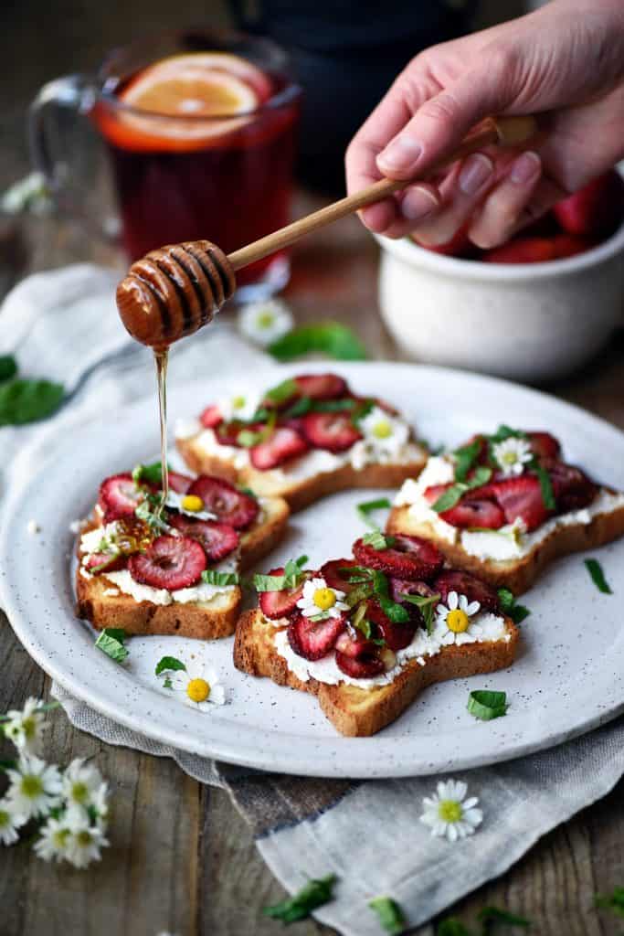 Drizzling honey onto toast topped with ricotta and roasted strawberries