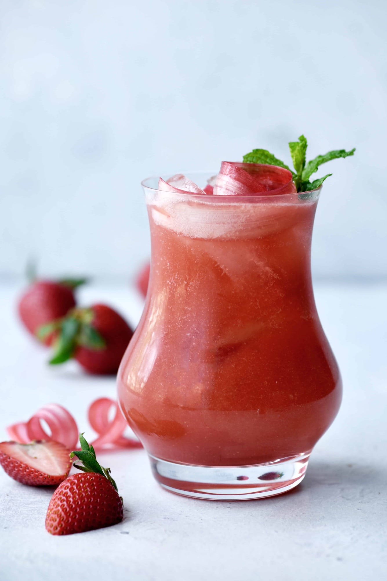 Side view of strawberry rhubarb daiquiri in a curved glass garnished with rhubarb ribbons