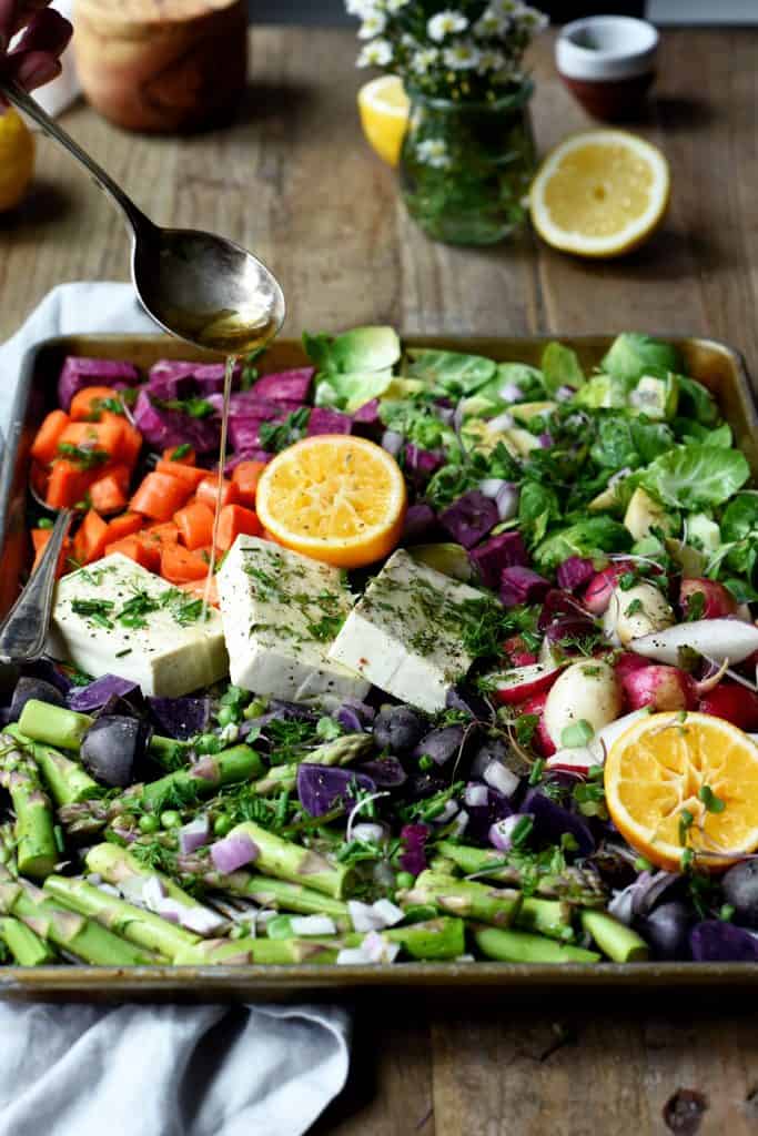 Drizzling olive oil onto sheet pan of roasted spring vegetables and tofu