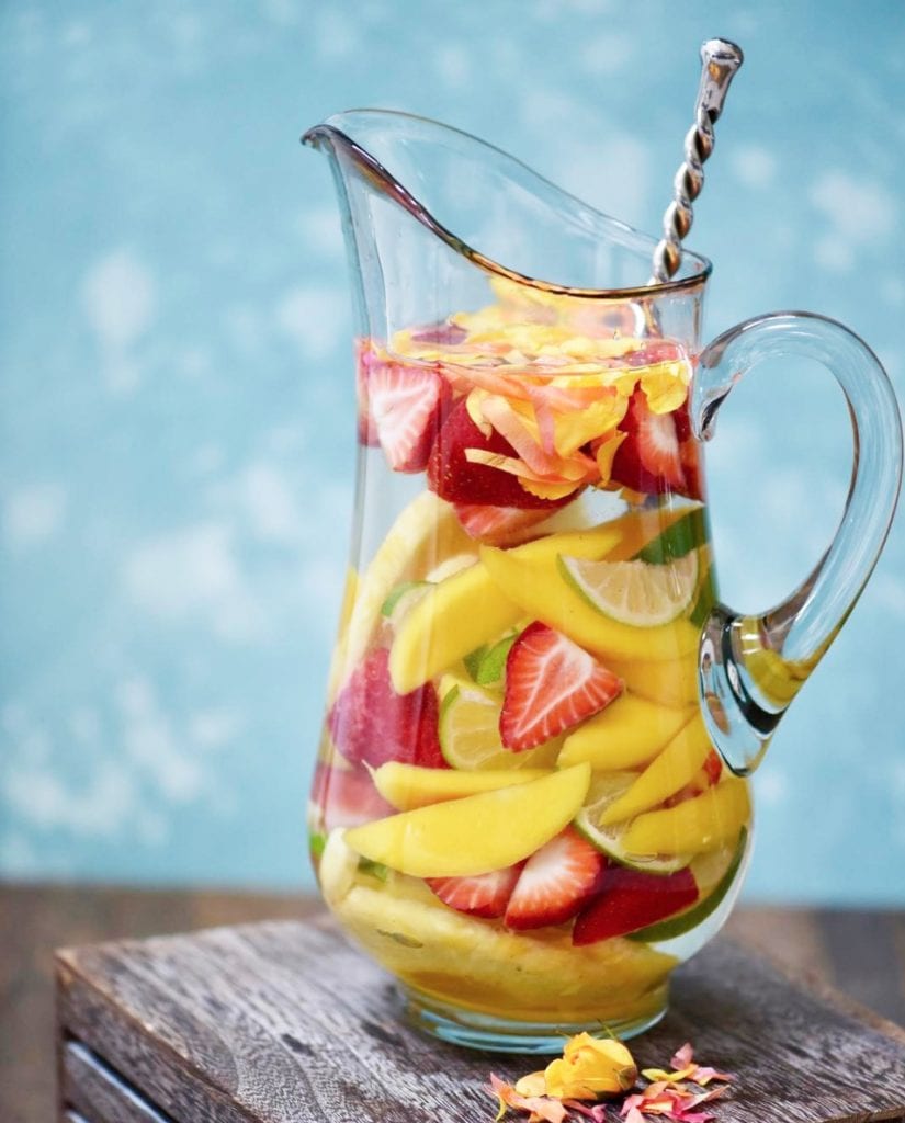 Large pitcher of mango, strawberry and lime infused water with blue background