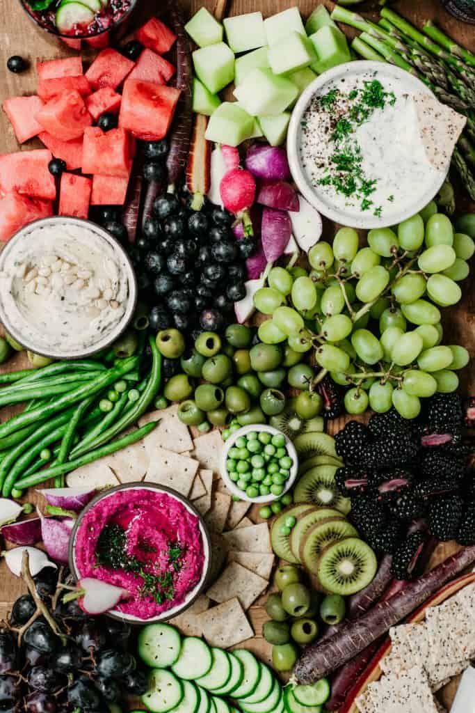 Close up of Overhead of snack platter on huge wood board with pink, purple and green vegetables