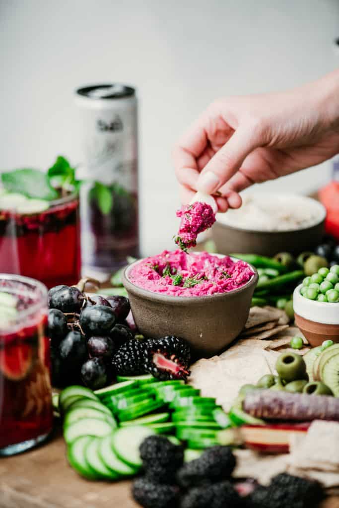 Side view of dipping radish into bright pink beet hummus