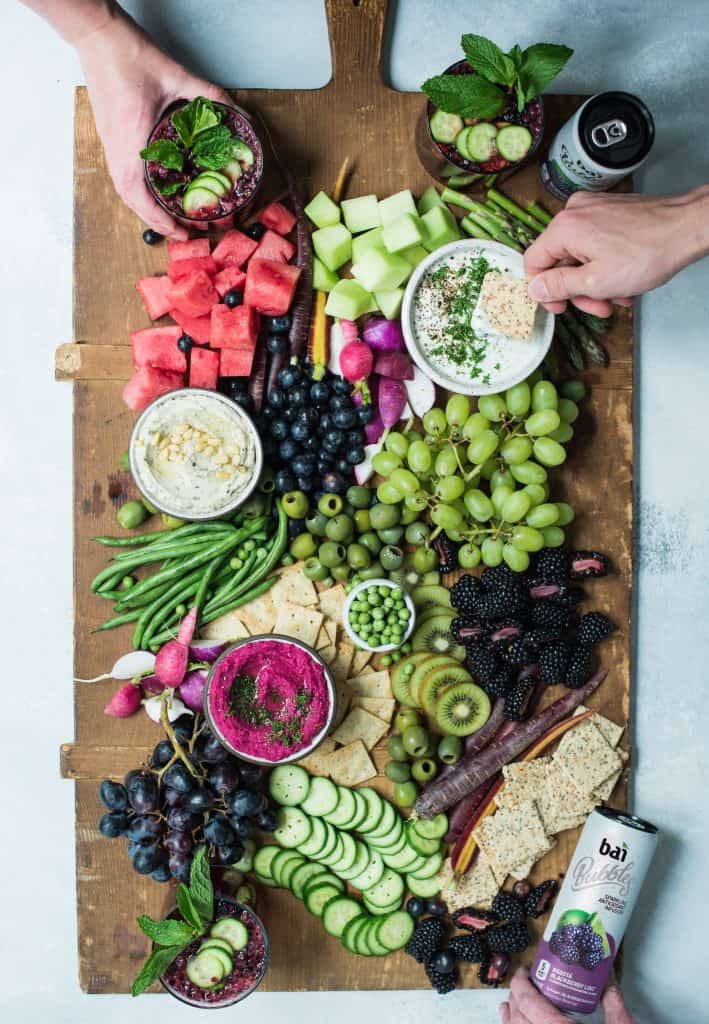 Overhead of snack platter on huge wood board with pink, purple and green vegetables