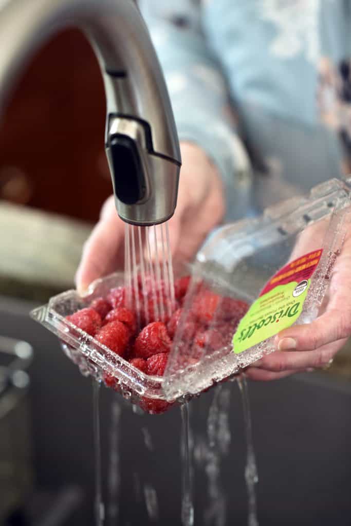 Container of Driscoll's raspberries being washed in sink
